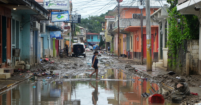 Woman walking through flooded street between damaged buildings in Honduras