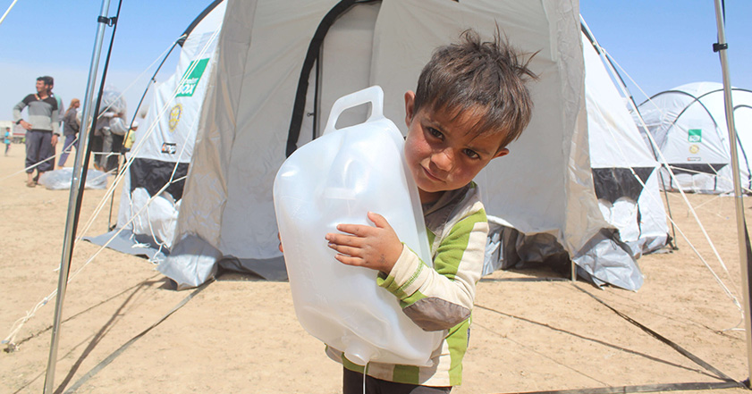 Boy in front of tent holding water carrier