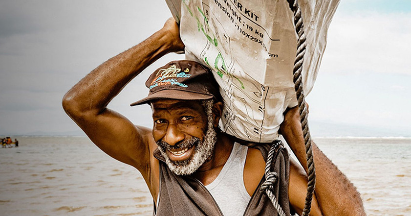 Man carrying shelter kit next to sea in Vanuatu
